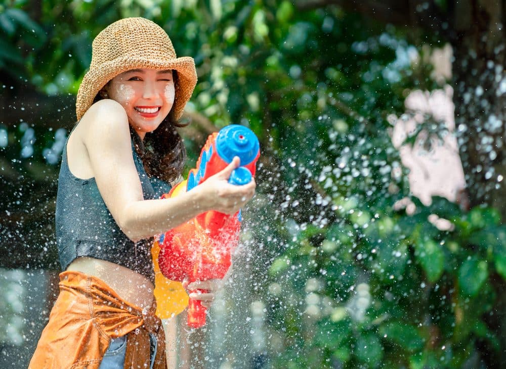 Smiling Asian woman was splashed by water. She is using a water gun for Songkran Festival. ซอฟต์พาวเวอร์