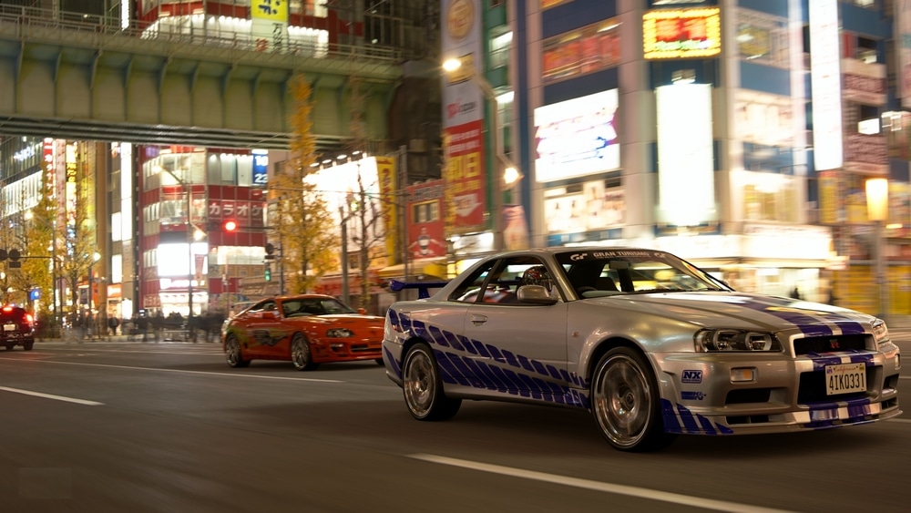 โตเกียว ญี่ปุ่น 9 เมษายน 2023 Nissan Skyline GTR 34 สีเทาและโตโยต้า Supra วิ่งบนถนนโตเกียวในตอนกลางคืน .