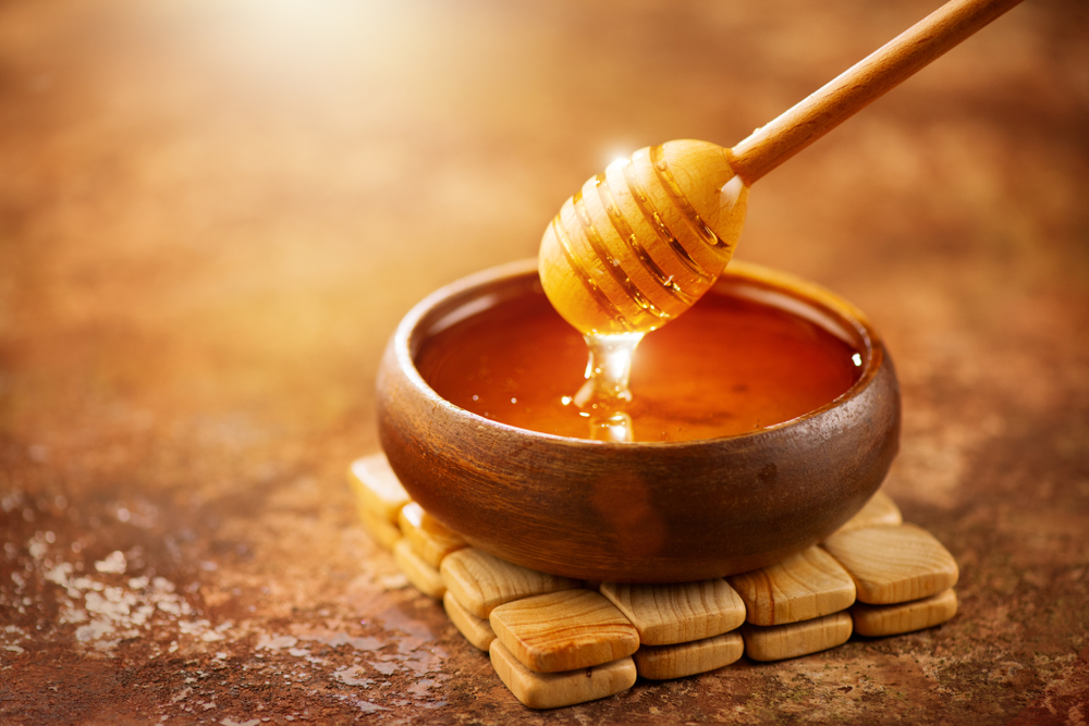 น้ำผึ้งหยดจากกระบวยน้ำผึ้งในชามไม้ ใกล้ชิด. น้ำผึ้งหนาอินทรีย์ที่มีสุขภาพดีจุ่มจากช้อนน้ำผึ้งไม้ปิด .