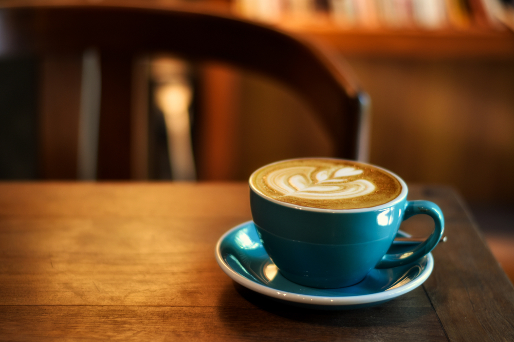กาแฟ ในถ้วยสีฟ้าบนโต๊ะไม้ในร้านกาแฟที่มีพื้นหลังมีแสง