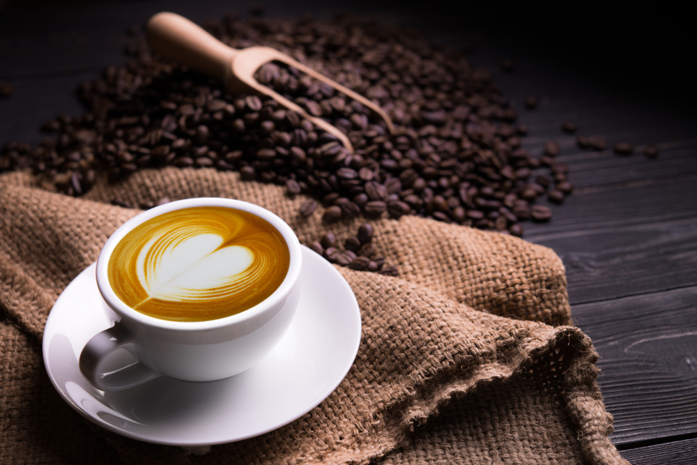 ลาเต้กาแฟสักแก้วที่มีรูปหัวใจและเมล็ดกาแฟบนพื้นไม้เก่าๆ
