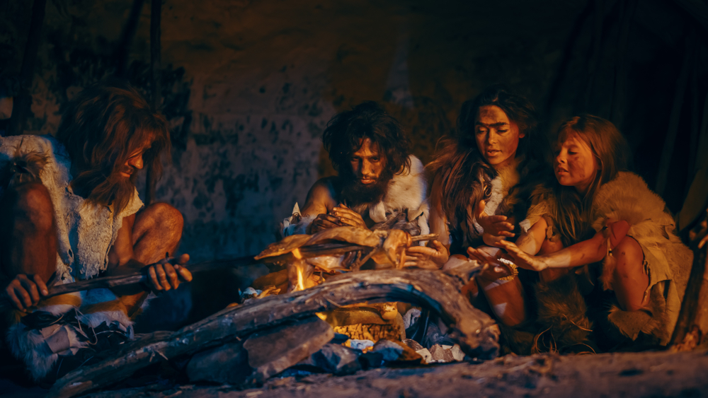 ครอบครัวนีแอนเดอร์ทัลหรือโฮโมซาเปียนส์ทำอาหารเนื้อสัตว์บนกองไฟแล้วกินมัน ชนเผ่านักล่ายุคก่อนประวัติศาสตร์สวมชุดสัตว์ย่างและกินเนื้อในถ้ำตอนกลางคืน วิวัฒนาการ