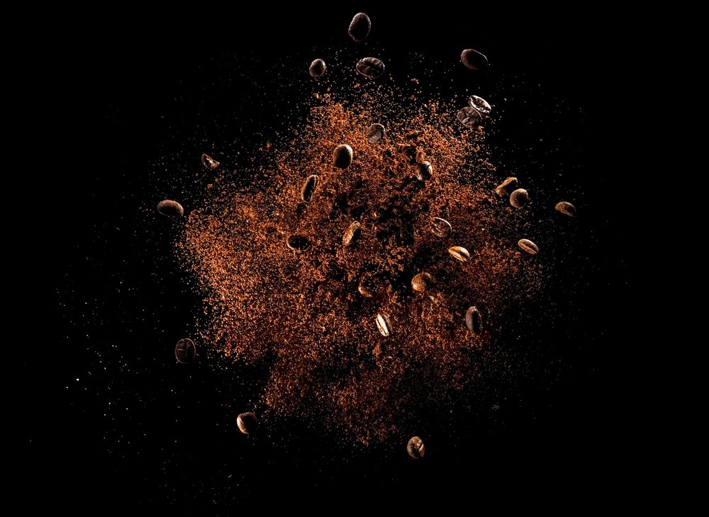 การระเบิดของ กาแฟ บดที่มีถั่วคั่วบนพื้นหลังสีดำ