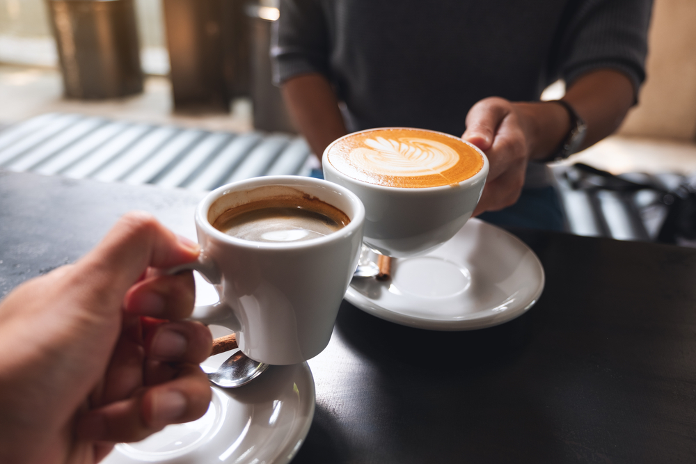 ภาพโคลสอัพของชายและหญิงกำลังชนแก้ว กาแฟ สีขาวในร้านกาแฟ